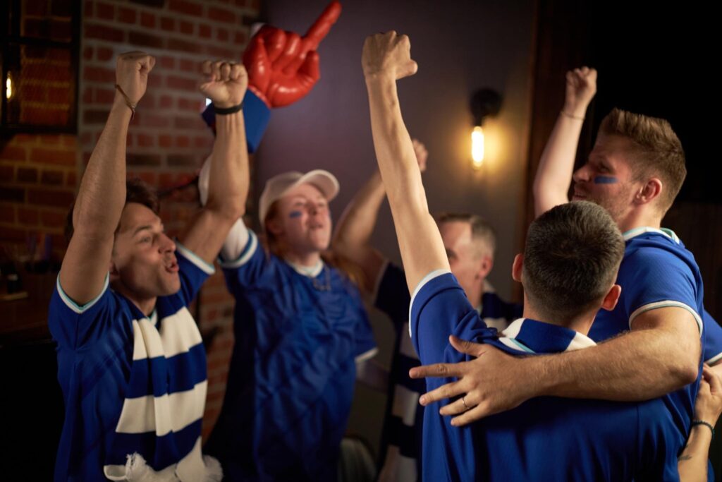 Torcedores de futebol comemorando vitória com braços levantados em bar
